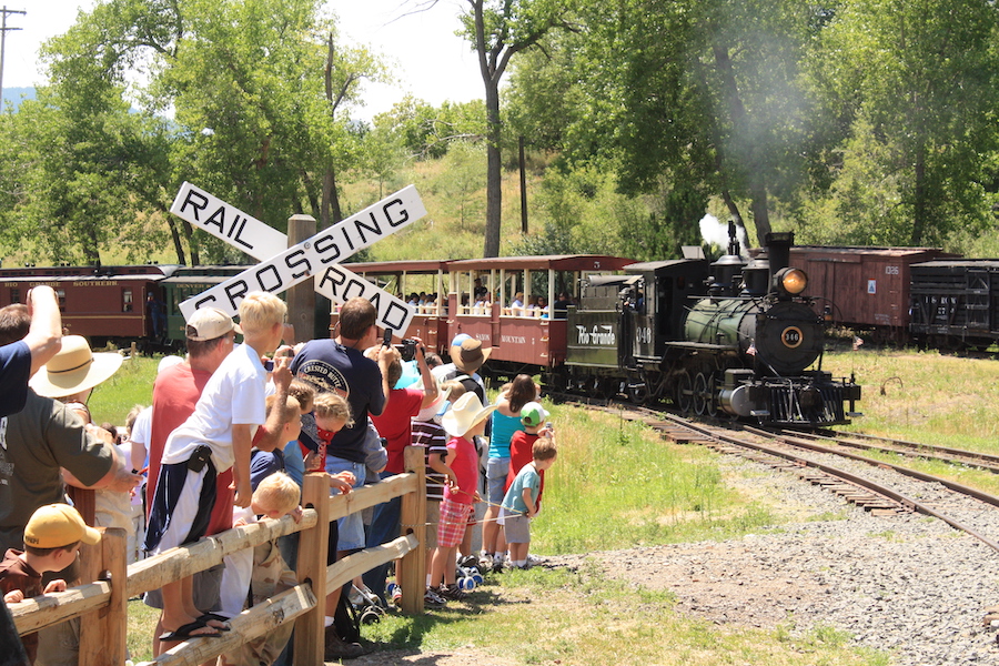 A group of adults and children watching a historic train approach at the Colorado Railroad Museum.