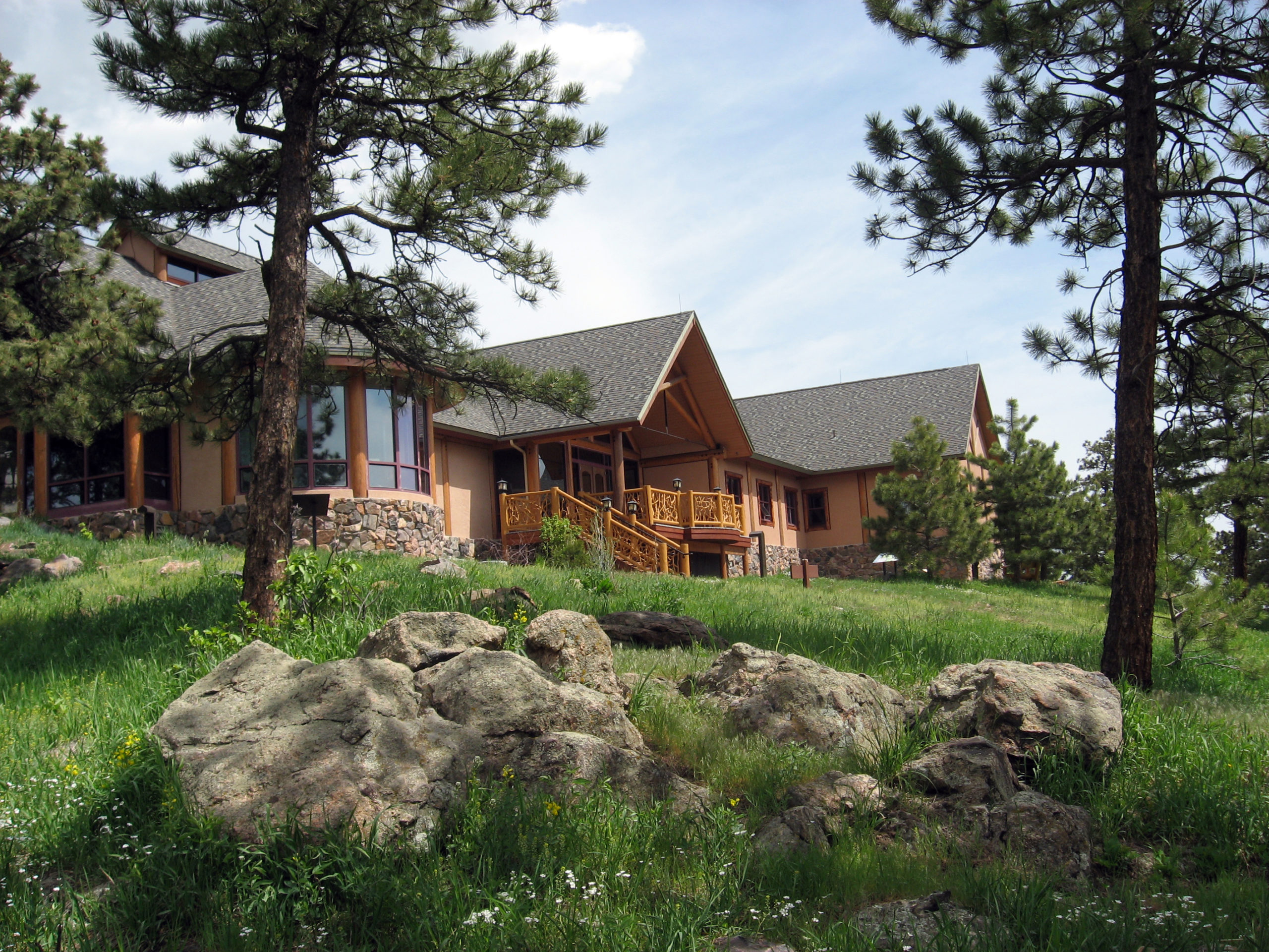 Mountain building with wood and stone accents on a sunny day with grass, large stones and evergreen trees.
