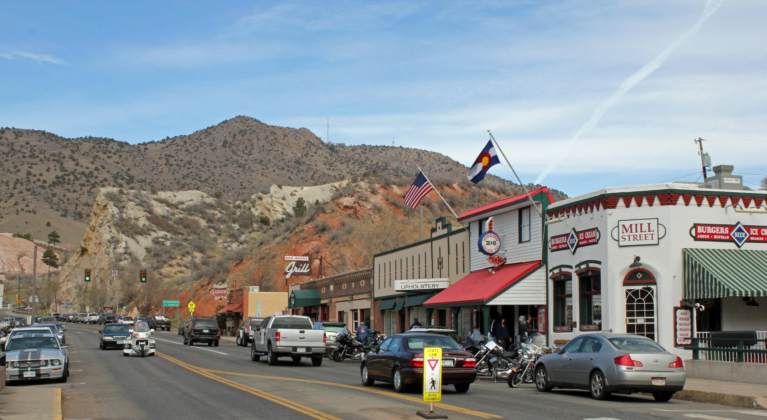 View of the historic district of the town of Morrison, Colorado with historic buildings that house shops and restaurants with mountains in the distance.