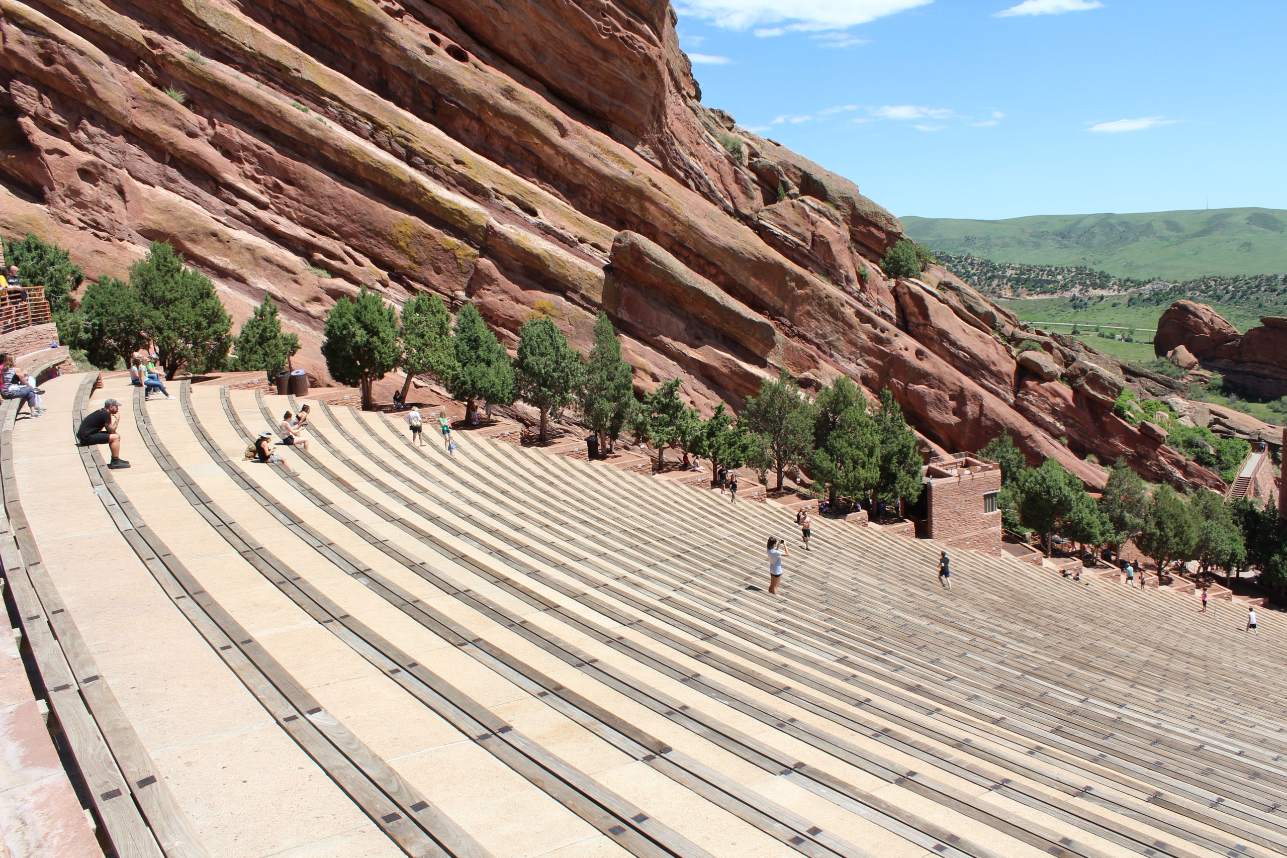 A number of people at Red Rocks Amphitheater on steps, looking down toward the stage with a high red rock wall to the left of the stairs.