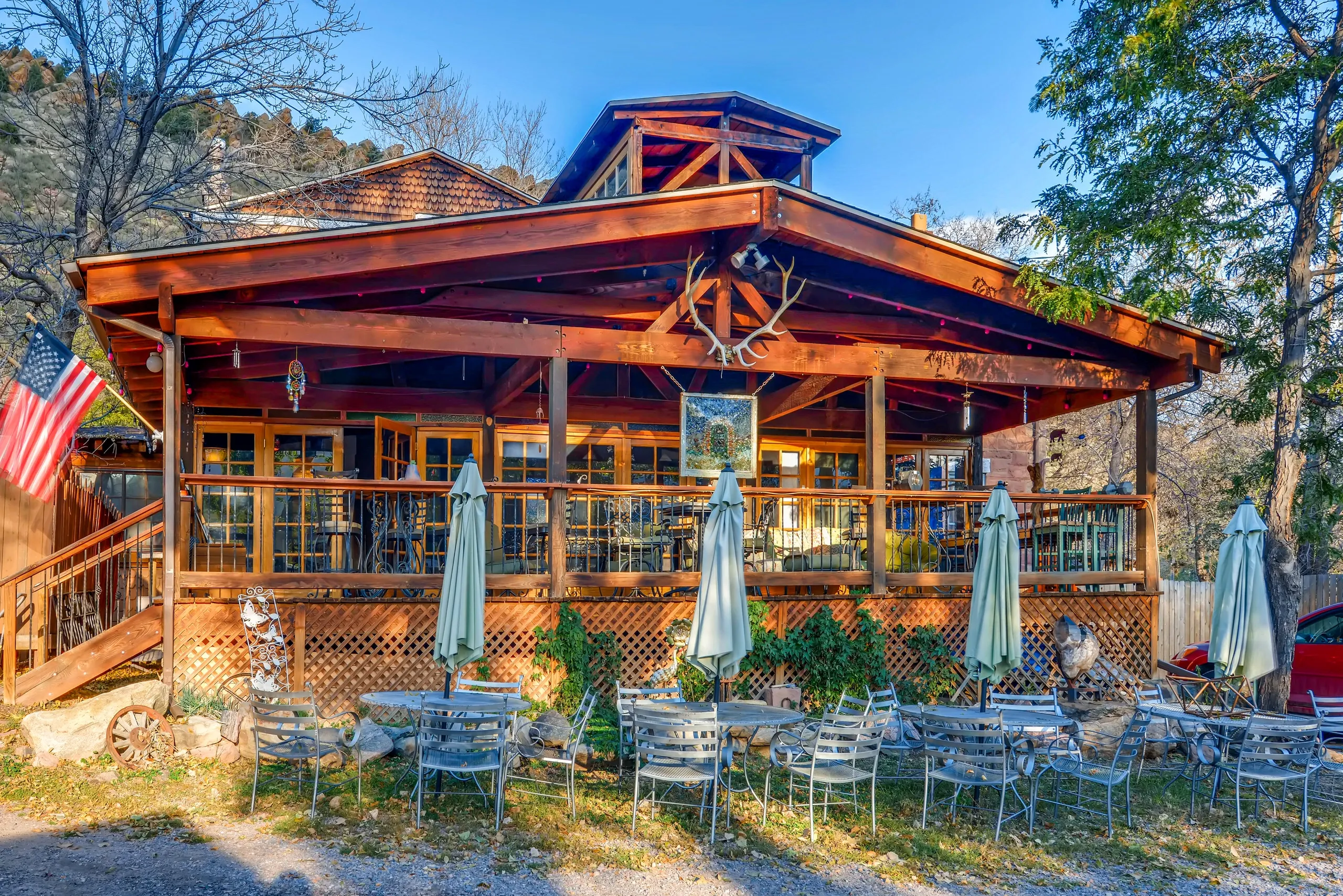 Exterior image of Cliff House Lodge in Morrison, Colorado that has wooden architecture and a porch with tables and chairs for dining on the porch and on the grass in front of the building.
