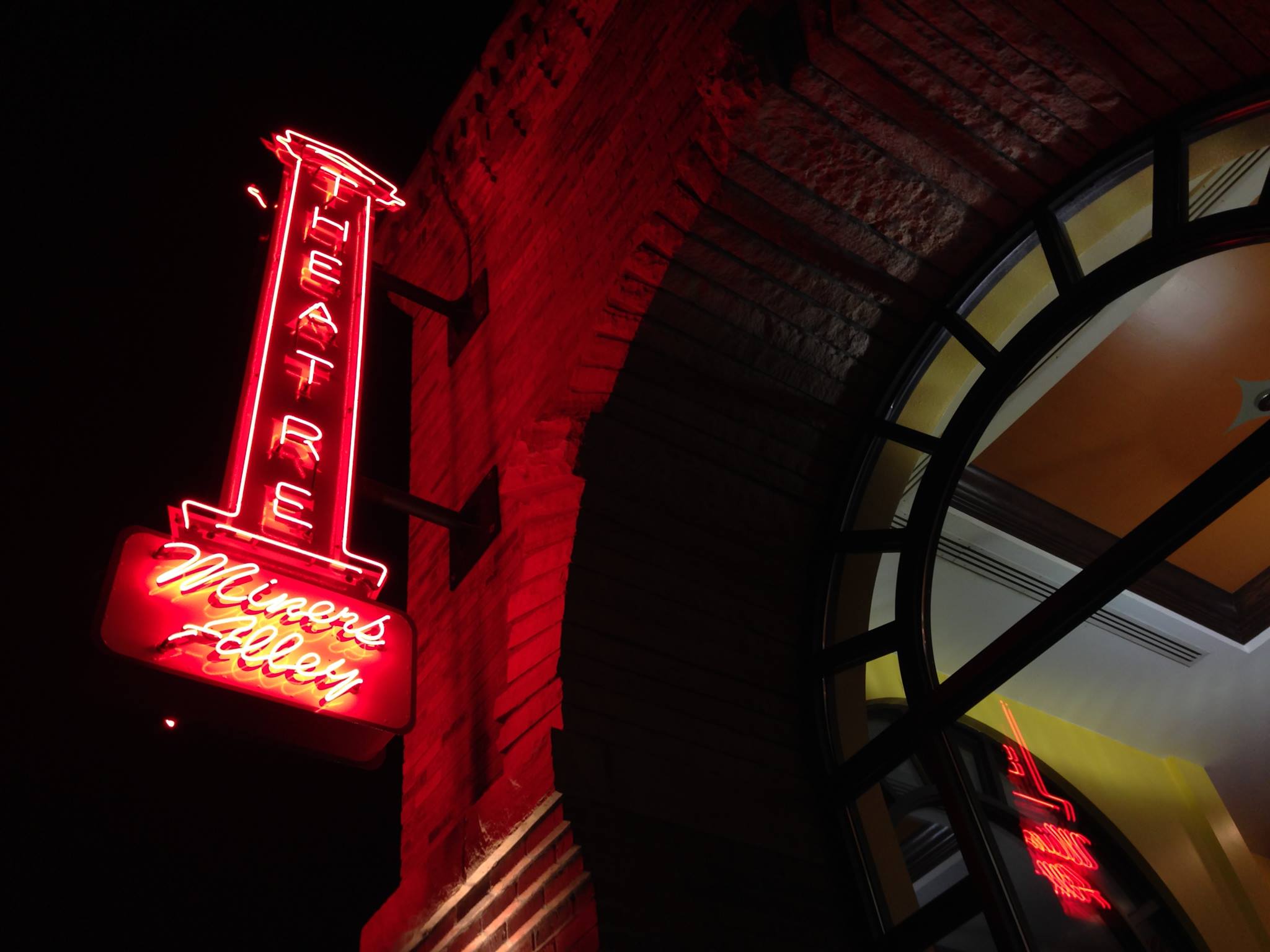 Sign for Miners Alley Theater lit up in red on the exterior of a brick building at night.