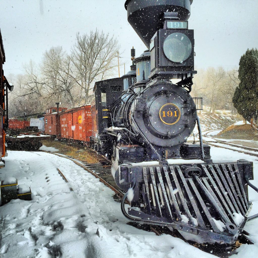 Black historic train in the winter with snowflakes falling from the sky.