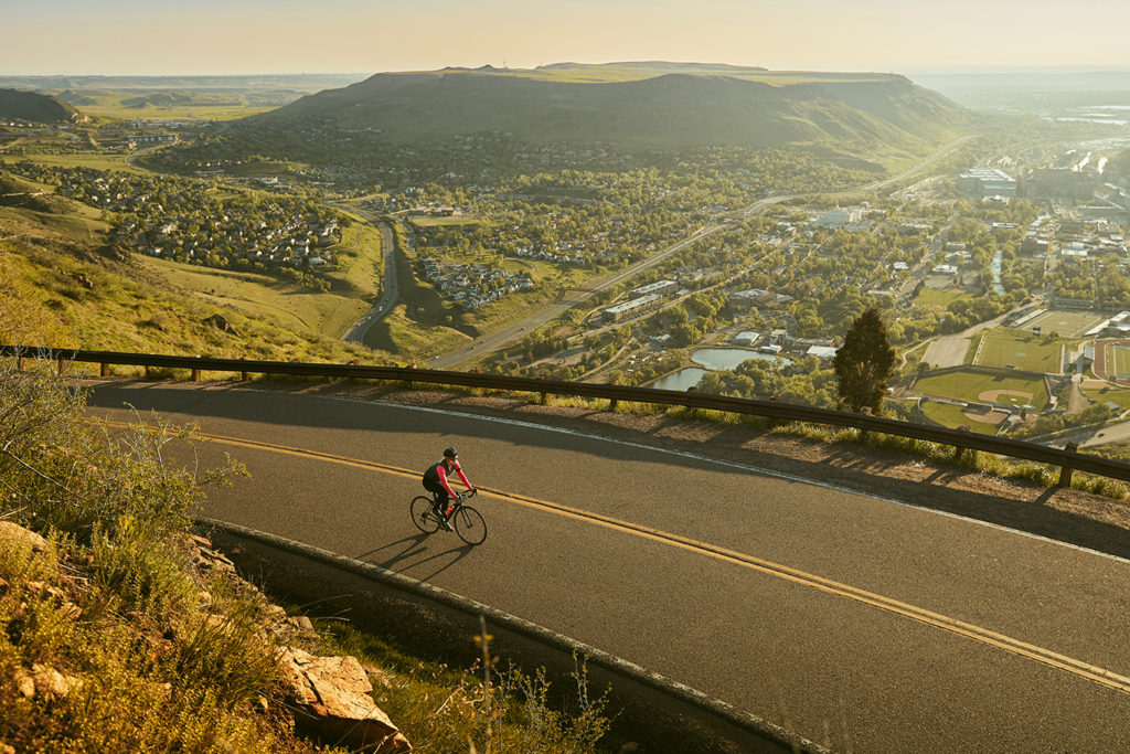 Person riding a bike on the road at sunset with a mountain in the distance.