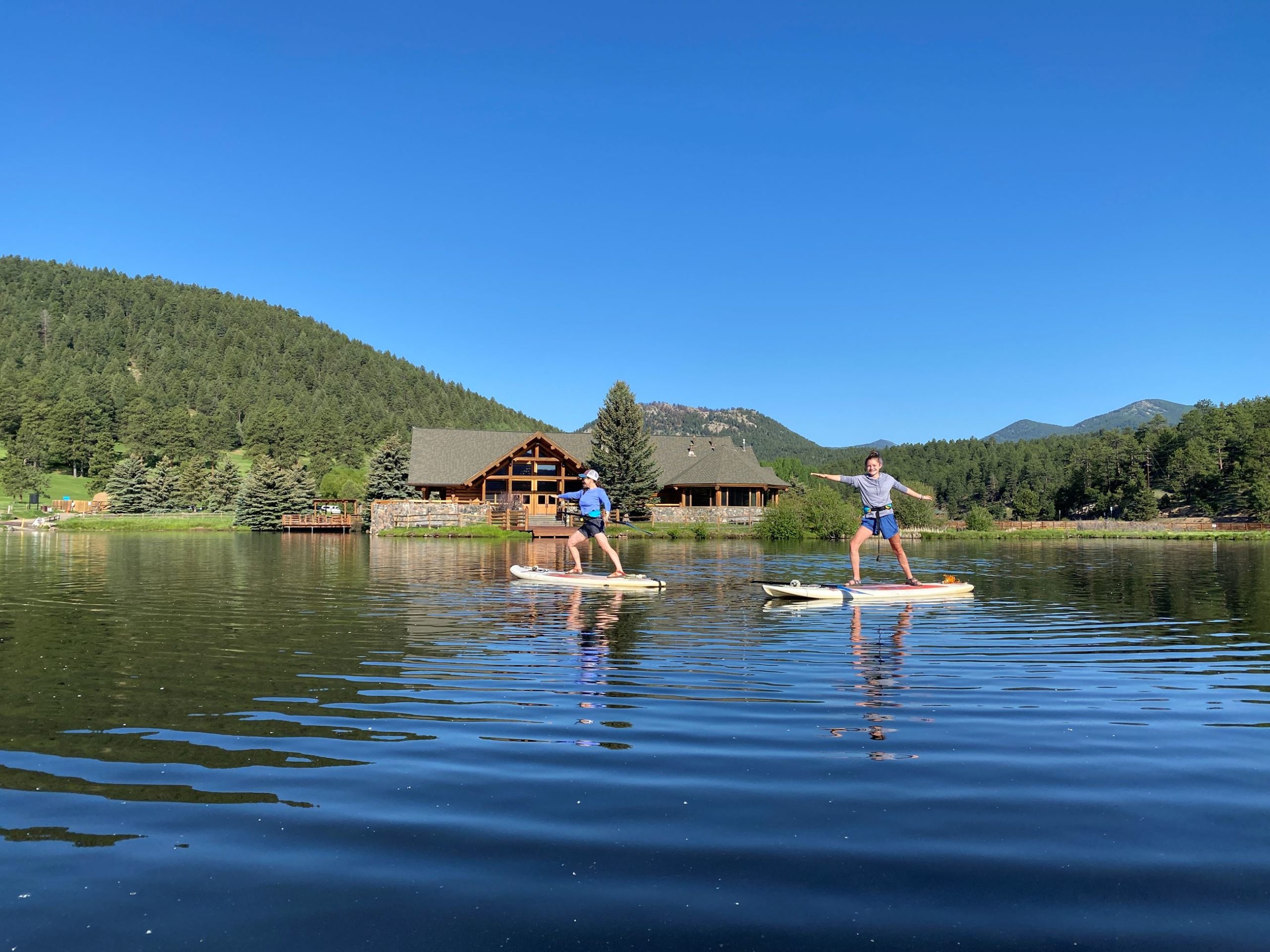 Two people doing stand up paddle boarding on Evergreen Lake in Colorado.