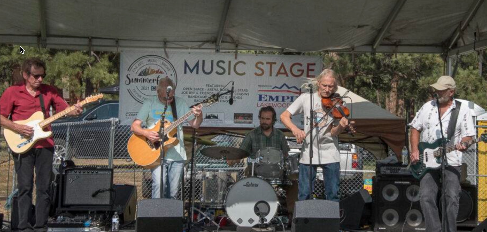 Group of 5 people playing music on a stage at a festival.