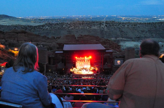 View between two people of Red Rocks Amphitheatre stage in Morrison, Colorado at dusk.