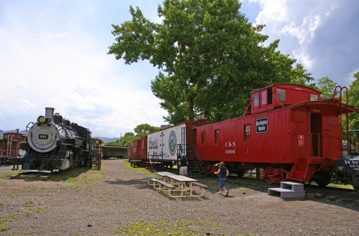 Historic red and black trains at the Colorado Railroad Museum on a sunny day outdoors.
