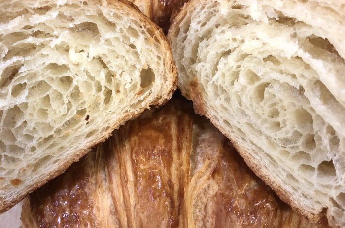 Multiple freshly baked croissants on a brown background. One croissant is cut open, showing the inside.