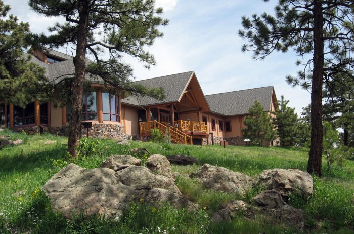 Mountain building with wood and stone accents on a sunny day with grass, large stones and evergreen trees.