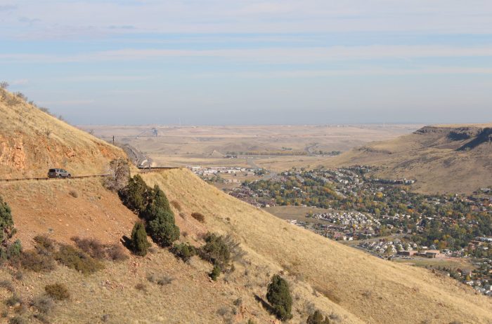 View of an SUV driving on the Lariat Trail from Windy Saddle Park in Colorado with a town in the distance.