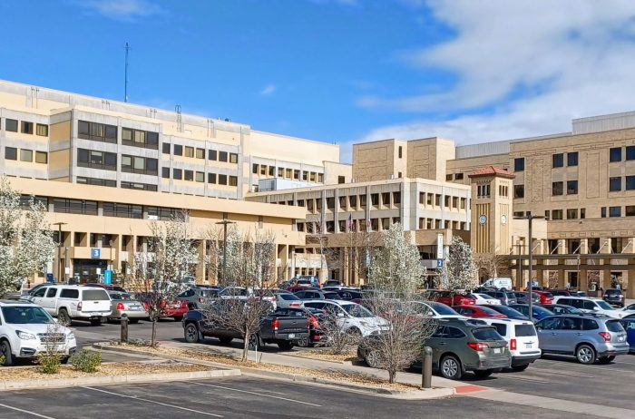 Large, light tan hospital building with many cars in the parking lot outside.