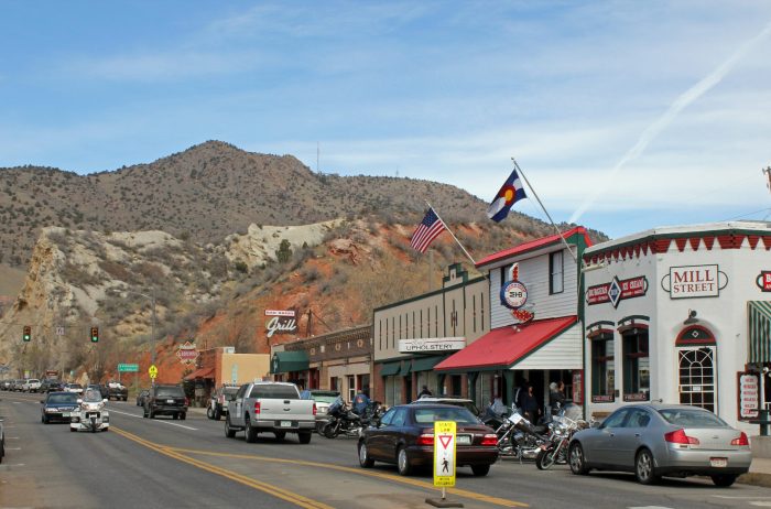 View of the historic district of the town of Morrison, Colorado with historic buildings that house shops and restaurants with mountains in the distance.