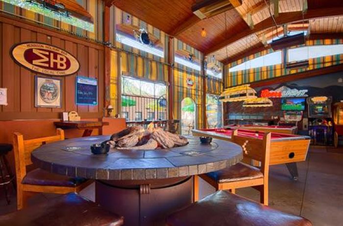 Interior of a cool restaurant with a fire pit, pool tables, and arcade games on the far wall.