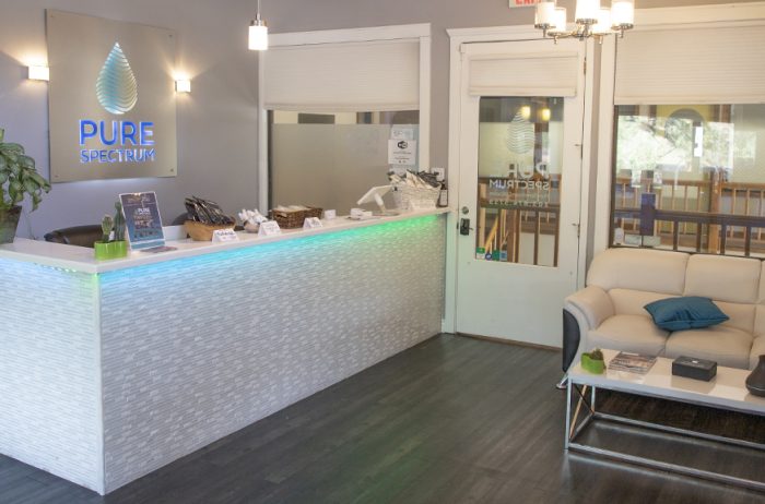 Interior of an attractive office reception area in light colors with the Pure Spectrum logo behind a tiled reception desk.