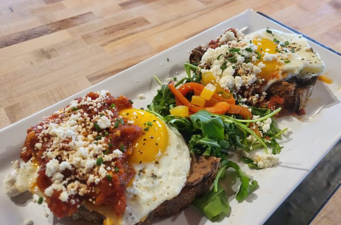 Tasty Egg dish with arugula salad on a rectangular white plate on a light wood background.