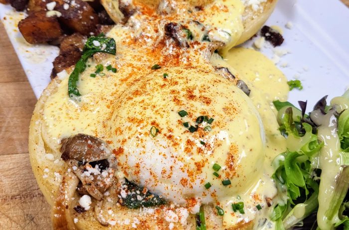 Tasty looking plate of eggs benedict with home fries and salad greens.